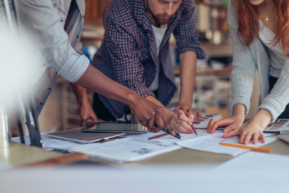 Stock-Photo-People-Around-Table-with-Papers People around desk looking at architectural outlines
